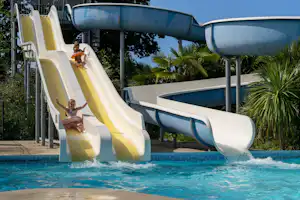 Wasserrutschen am Campingplatz über einem Pool, mit blauem Rutschkanal und Spritzwasser im Vordergrund.