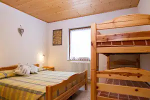 Doppelbett und Etagenbett im hellen Campingzimmer mit Holzdecke, Fenster und Heizkörper am Rand.