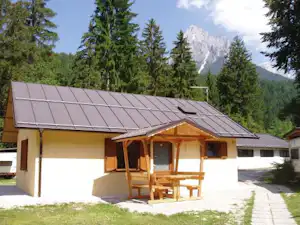 Ferienhaus mit Solardach, Holzveranda und Tisch vor dem Eingang, umgeben von Nadelbäumen und Bergblick.
