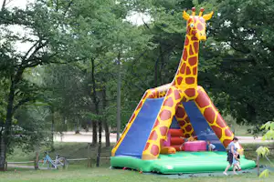 Gelbe Giraffen-Hüpfburg im grünen Park mit blauer Rutsche, daneben Fahrräder und Bäume.