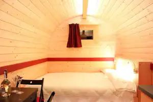 Gemütliches Holz-Chalet-Zimmer mit Doppelbett, Nachttisch und Lampen, seitlich ein Tisch mit Gläsern und Flasche.
