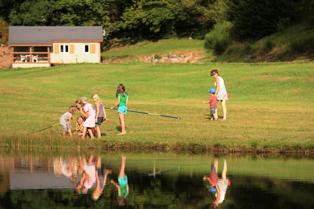 Camping Chalets de l'Eau Verte - Familie am See mit einem Chalet im Hintergrund