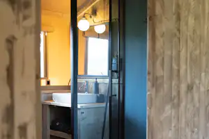 Badezimmer im Campingbereich mit Waschbecken, Spiegel und Beleuchtung, sichtbar durch eine offene Tür.