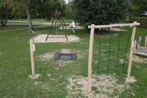 Spielplatz auf dem Campingplatz: Holzschaukel, Sandfläche und Rasen, umgeben von Bäumen und Hecken.