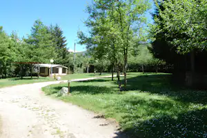 Zeltstellplatz im Grünen mit Vorzelt, Holzüberdachung, Kiesweg und Bäumen auf dem Campingplatz.