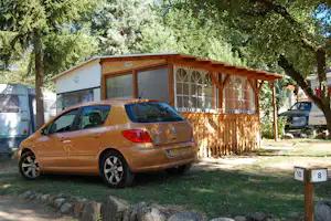 Wohnwagen mit Holzcarport, davor geparkter Pkw und Bäume im Hintergrund auf dem Campingplatz.