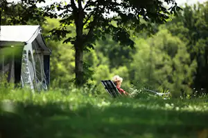 Camping Château le Verdoyer - Sitzender Camper vor dem Zelt auf der Wiese der Campingplatzanlage