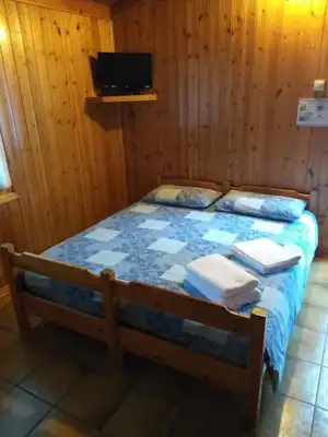 Bett in einer Holzunterkunft mit TV an der Wand, gefliester Boden und Kissen auf dem Bett.
