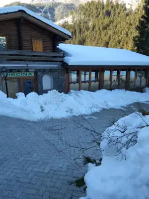Campinghaus im Winter mit verschneitem Vorplatz, Holzveranda und Blick auf Berge und Nadelwald.