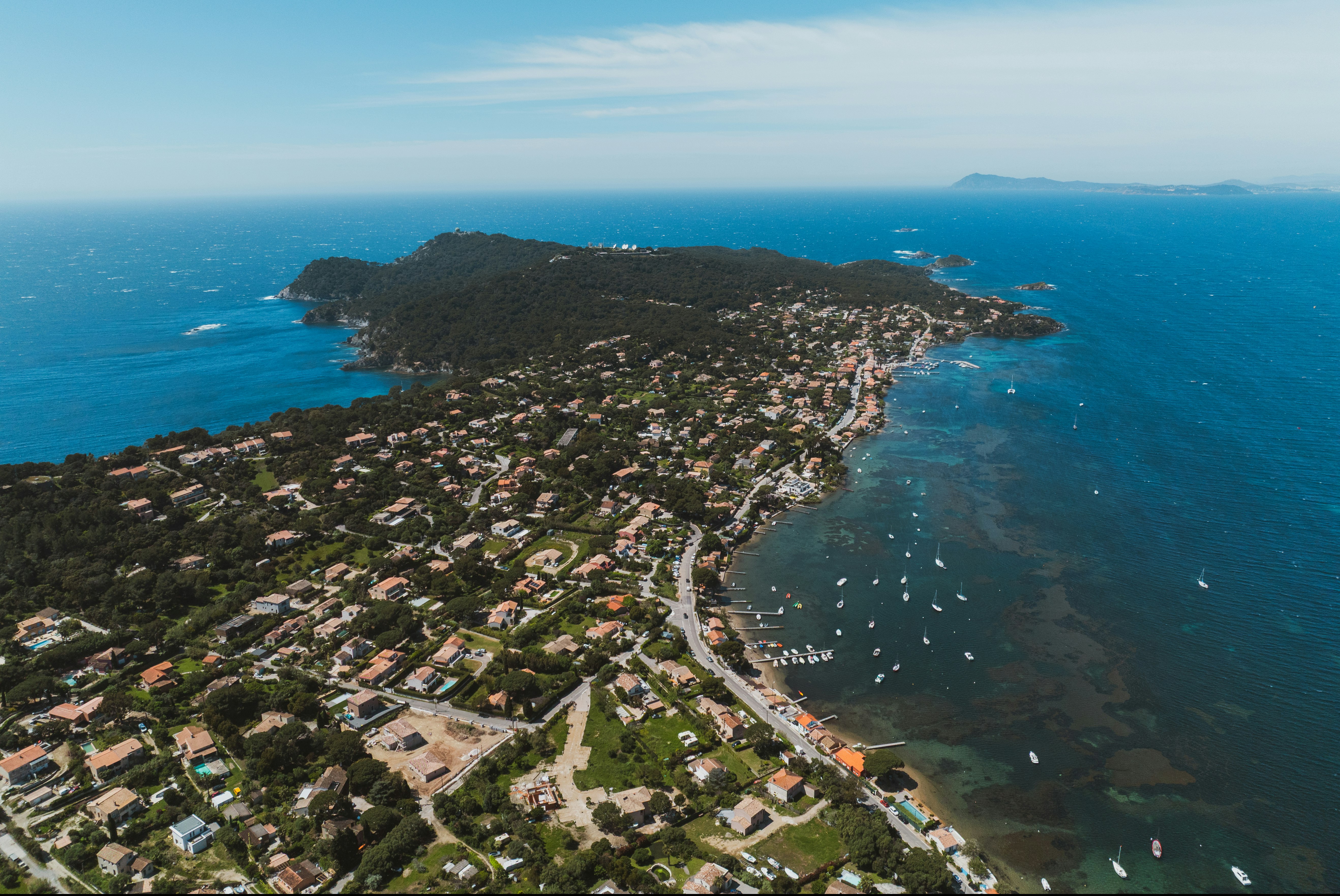 Luftaufnahme eines Küstenorts am Meer mit Häusern, Hafenbecken und Booten entlang der Bucht.