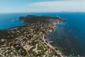 Luftaufnahme eines Küstenorts am Meer mit Häusern, Hafenbecken und Booten entlang der Bucht.
