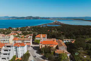 Blick von oben auf ein Küstendorf mit Häusern und roten Dächern, Straße und Meerbucht im Hintergrund.