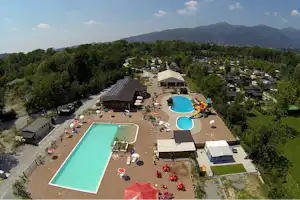 Luftaufnahme eines Campingplatzes mit großem und kleinem Schwimmbecken, Sonnenschirmen, Spielbereich und Blick auf bewaldete Berge.