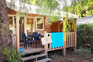 Holzterrasse am Campingplatz mit Sitzgruppe, Tisch und Stühlen, daneben Wäscheleine und Hecke im Gartenbereich.