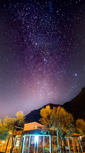 Wohnwagen auf einem Campingplatz bei Nacht, davor Zaun und Bäume, darüber ein klarer Sternenhimmel.
