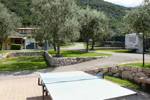 Wohnwagen und Wohnmobil auf einem Campingplatz, gepflasterter Weg, Steinmauer und Bäume im grünen Tal.