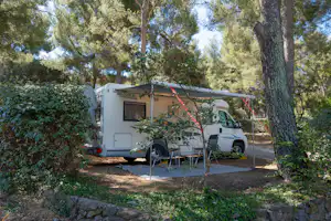 Wohnmobil auf Stellplatz im Grünen, mit Vorzelt und Tisch, umgeben von Olivenbäumen und Hecken.