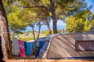 Campingzelt im Wald mit Wäscheleine und bunten Tüchern, im Hintergrund Bäume und ein Blick ins Tal.