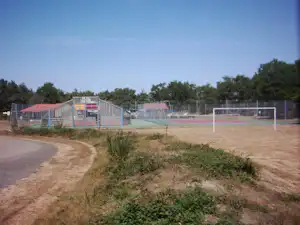 Sportplatz mit Tennisfeldern und Umzäunung auf dem Campinggelände, daneben ein Weg und Büsche am Rand.