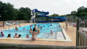 Schwimmbecken auf dem Campingplatz mit blauen Wasserrutschen, Liegen am Beckenrand und mehreren Personen im Wasser.