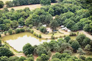 Campingplatz am See im Grünen, mit Uferweg, kleinen Gebäuden und Wohnwagen zwischen Bäumen in ruhiger Landschaft.