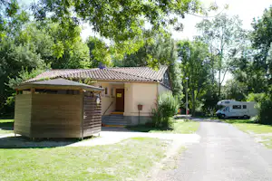 Campinghaus mit Holzschuppen, Terrasse und Treppe; daneben Wohnmobil auf dem Stellplatz im Grünen.