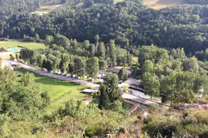 Blick auf einen Campingplatz im grünen Tal mit Straße, Bäumen, Wiesen und mehreren kleinen Gebäuden.