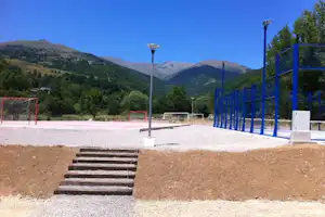 Sportplatz auf einem Campinggelände mit Fußballtoren, Kiesboden und Blick auf grüne Berge in der Ferne.
