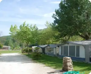 Reihen von Wohnwagen und Zelten auf einem Campingplatz, mit Grasfläche, Bäumen und einem Weg entlang der Stellplätze.