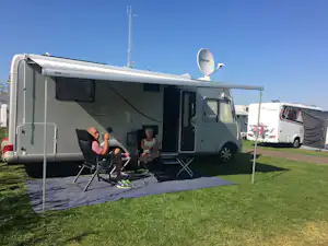 Wohnmobil mit Vorzelt und Sitzgruppe auf einem Campingplatz, Rasenfläche und weitere Wohnmobile im Hintergrund.