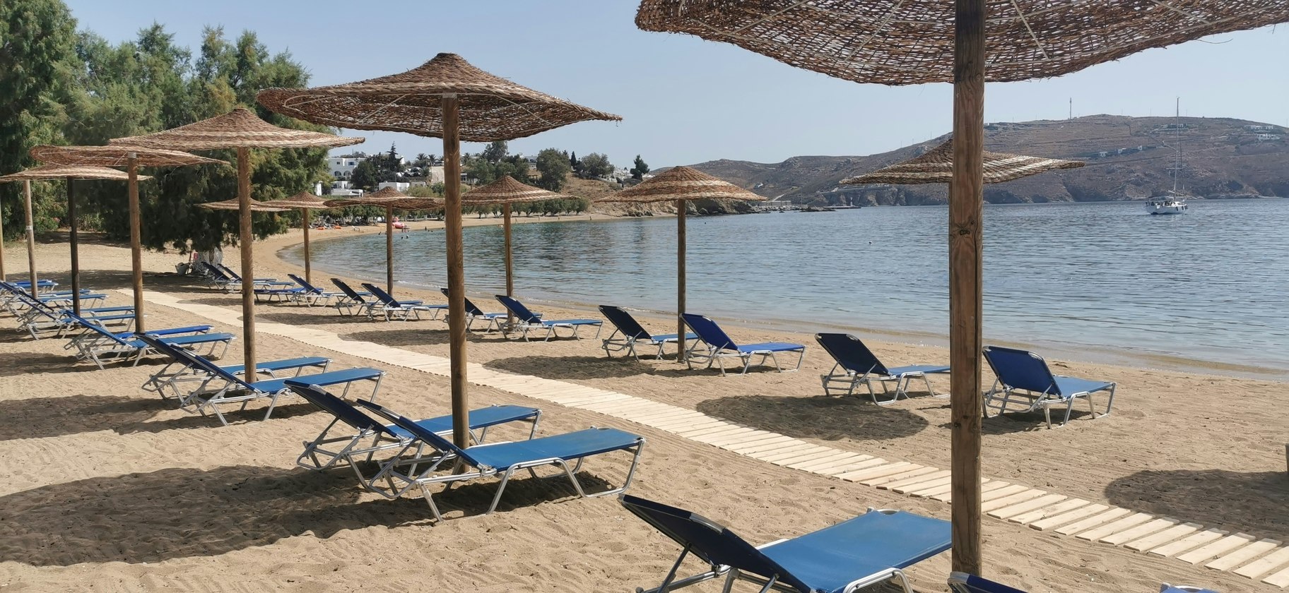 Sonnenliegen am Seeufer unter Sonnenschirmen, Holzsteg und Wasser im Hintergrund, am Campingplatz.
