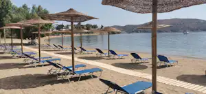 Sonnenliegen am Seeufer unter Sonnenschirmen, Holzsteg und Wasser im Hintergrund, am Campingplatz.