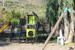 Campingplatz mit Holzzaun und Sitzbank, im Hintergrund grüne Hügel und Bäume, daneben ein kleines Zeltgestell.