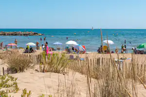 Campingzelte und Sonnenschirme am Sandstrand, im Hintergrund das türkisfarbene Meer und einzelne Badegäste.