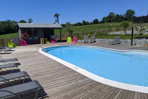 Schwimmbecken auf einer Holzterrasse mit Liegestühlen, Sonnenschirmen und Blick auf Wiese und Bäume am Campingplatz.
