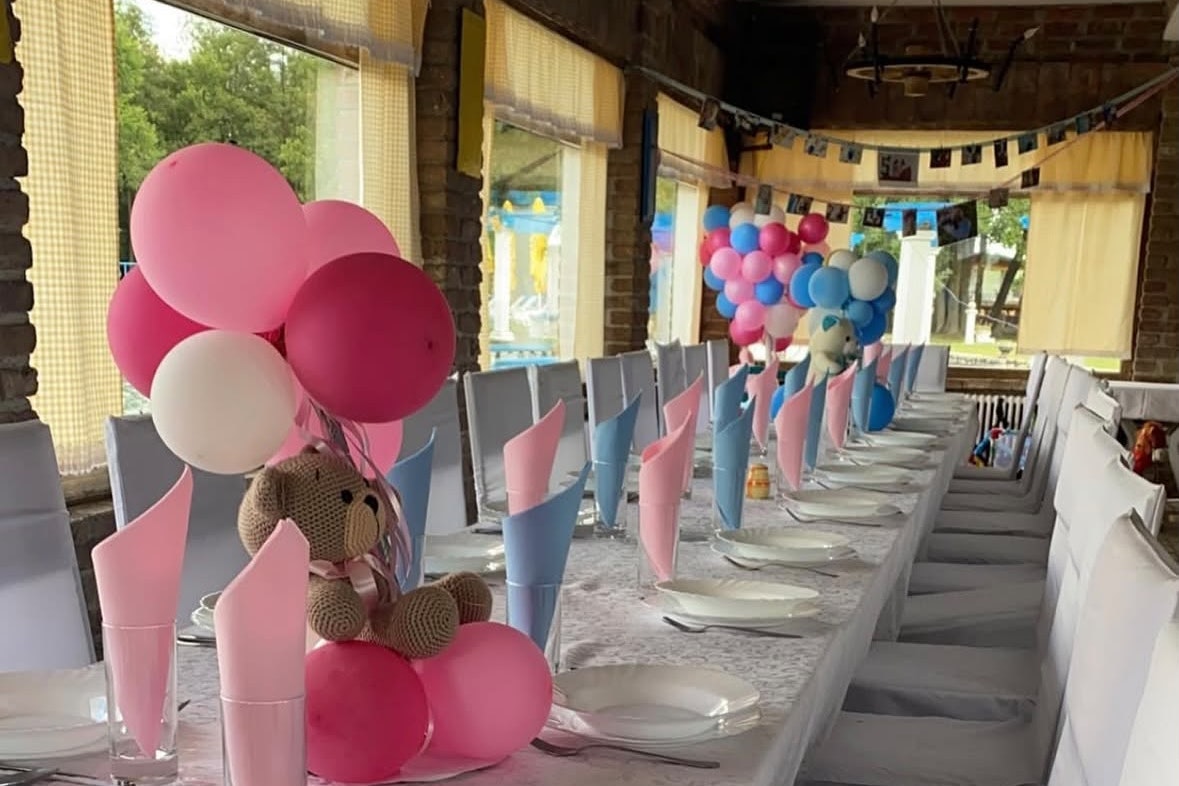 Festlich gedeckter Tisch im Zeltbereich mit rosa Luftballons, bunten Girlanden und Stühlen entlang der langen Tafel.