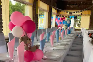 Festlich gedeckter Tisch im Zeltbereich mit rosa Luftballons, bunten Girlanden und Stühlen entlang der langen Tafel.