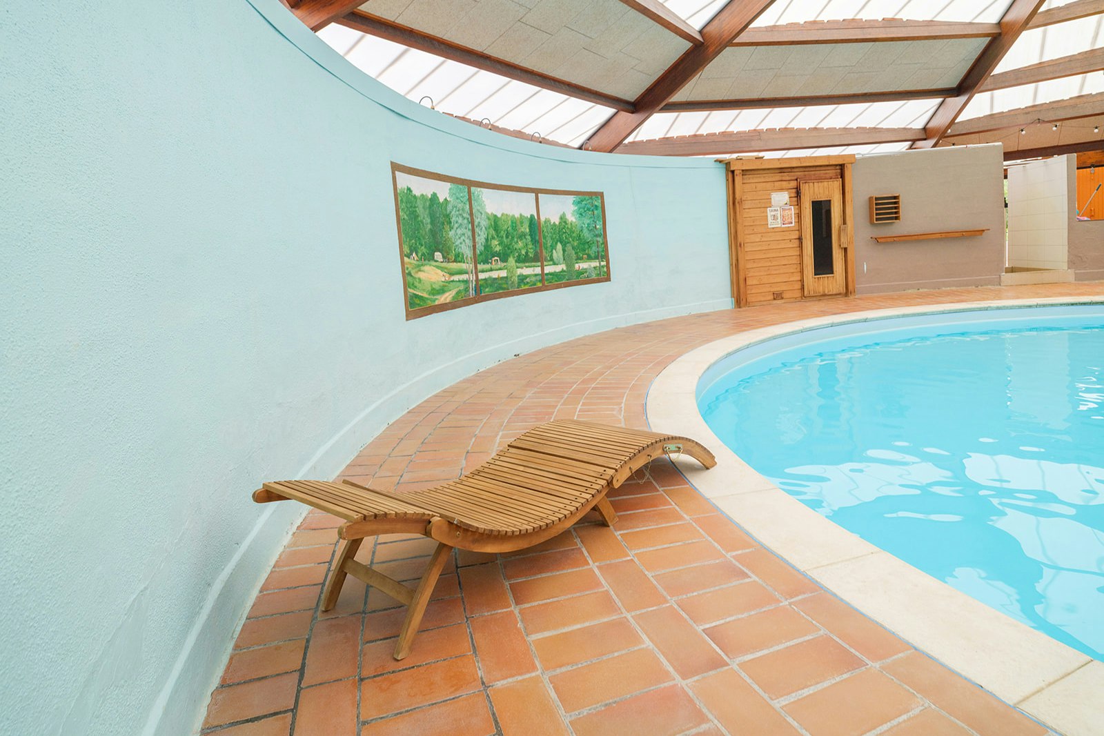 Sonniger Innenhof mit Fliesenboden, Liegestuhl und rundem Pool neben einer hellen Wand und Holztür am Gebäude.