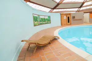 Sonniger Innenhof mit Fliesenboden, Liegestuhl und rundem Pool neben einer hellen Wand und Holztür am Gebäude.
