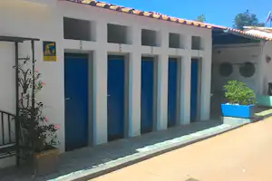 Reihen von Türen an einem Campinggebäude, davor eine Terrasse mit Pflanzkübeln und Pflanzen im Vordergrund.