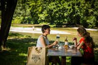 Camping Cévennes Provence - Camperinnen beim essen an einer Bank mit dem Fluss im Hintergrund