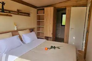 Schlafzimmer in einem Mobilheim: zwei Betten, Holzregale und Schranktüren, daneben eine offene Tür ins Zimmer.