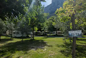 Campingplatz mit Wohnwagen und Bungalows, Bäume im Vordergrund und Blick auf die Berge, Schild „Camping Daino“.