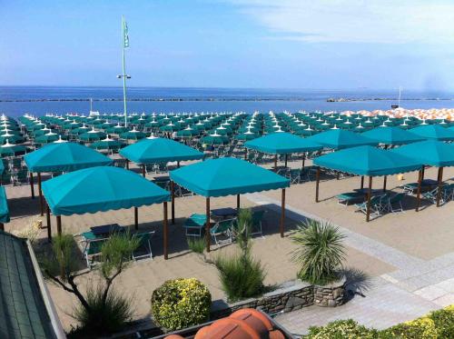 Reihe von türkisfarbenen Sonnenschirmen und Liegen am Strand, mit Wegen und Pflanzen im Campingbereich.