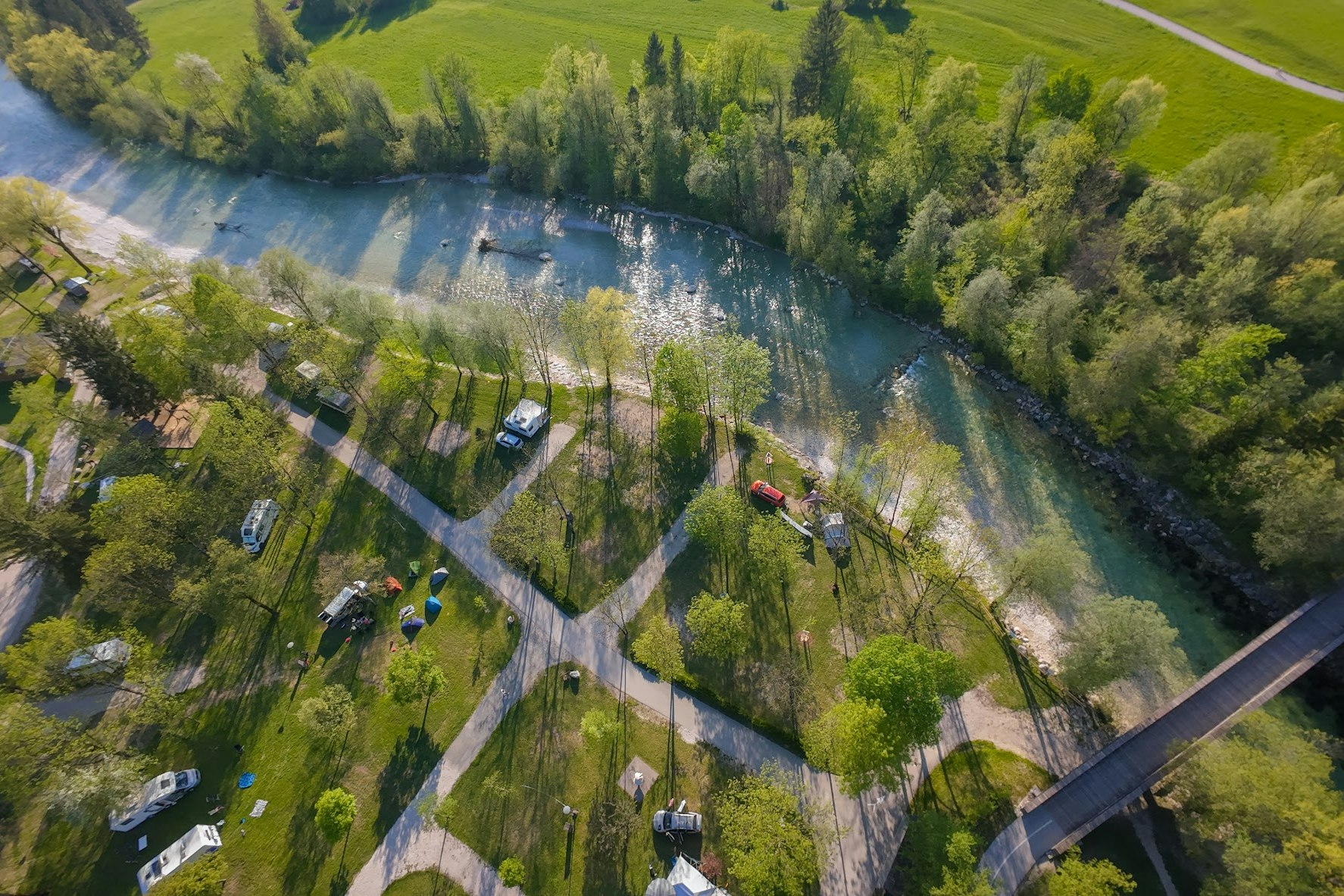 Luftaufnahme eines Campingplatzes am Fluss mit Wohnwagen, Wegen und Bäumen entlang des Ufers.