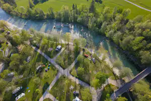 Luftaufnahme eines Campingplatzes am Fluss mit Wohnwagen, Wegen und Bäumen entlang des Ufers.