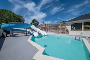 Beheizter Camping-Pool mit Sonnenschirm, Liegen und Blick auf das Gebäude mit Fenstern und Geländer.