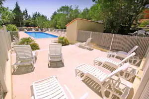 Poolbereich mit weißem Zaun, Liegestühlen und Sonnenschirmen auf der Terrasse, umgeben von Bäumen und Sträuchern.
