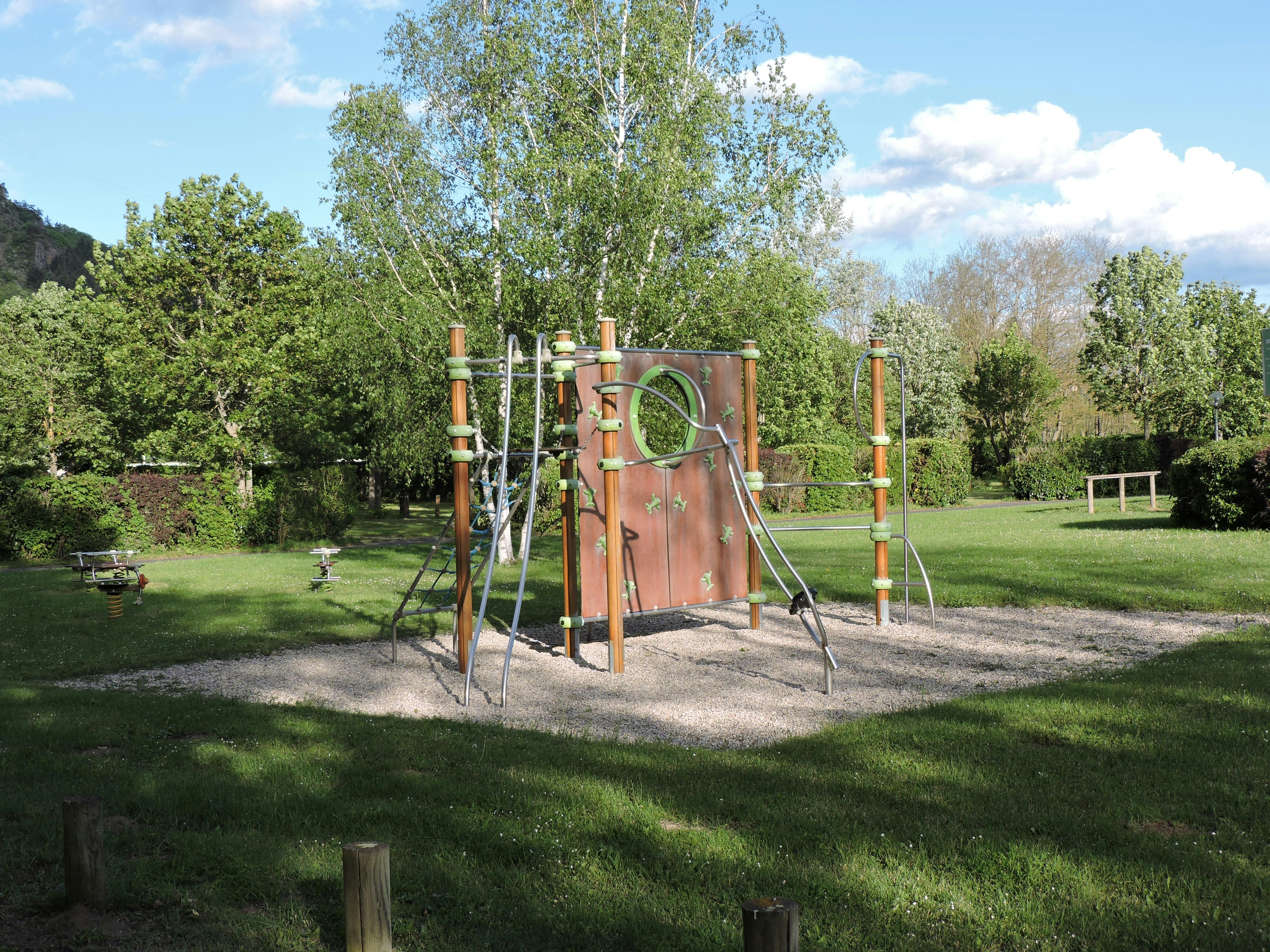 Spielplatz auf dem Campingplatz mit Klettergerüst, Rutsche und Sandfläche im grünen Garten mit Bäumen.