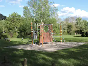Spielplatz auf dem Campingplatz mit Klettergerüst, Rutsche und Sandfläche im grünen Garten mit Bäumen.